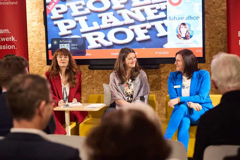Drei Frauen sitzen auf einem Bühnenpodium beim BVMW Unternehmerabend und diskutieren. Hinter ihnen zeigt eine große Leinwand "People, Planet, Profit" und Veranstaltungshinweise im futureoffice Karlsruhe - eingefangen von der Experten-Eventfotografie.