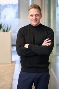 Businessfoto Mann mit schwarzem Pulli vor Modernem Bürohintergrund